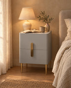 Narrow grey bedside table with a marble-effect top and gold legs with a lamp switched on, a book and reading glasses in the evening