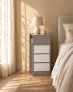 Narrow grey bedside table with a side shelf and three drawers in morning light