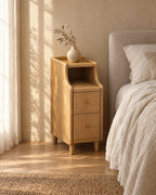 Three-quarter view of the narrow natural wood bedside table beside a bed