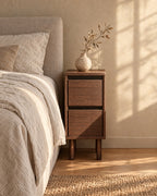 Three-quarter view of the narrow walnut-effect bedside table beside the bed