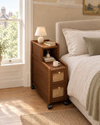 Narrow rattan bedside cabinet on castors beside a linen bed in a British bedroom