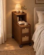 Narrow walnut and rattan bedside cabinet with a lamp switched on and an open book in the evening