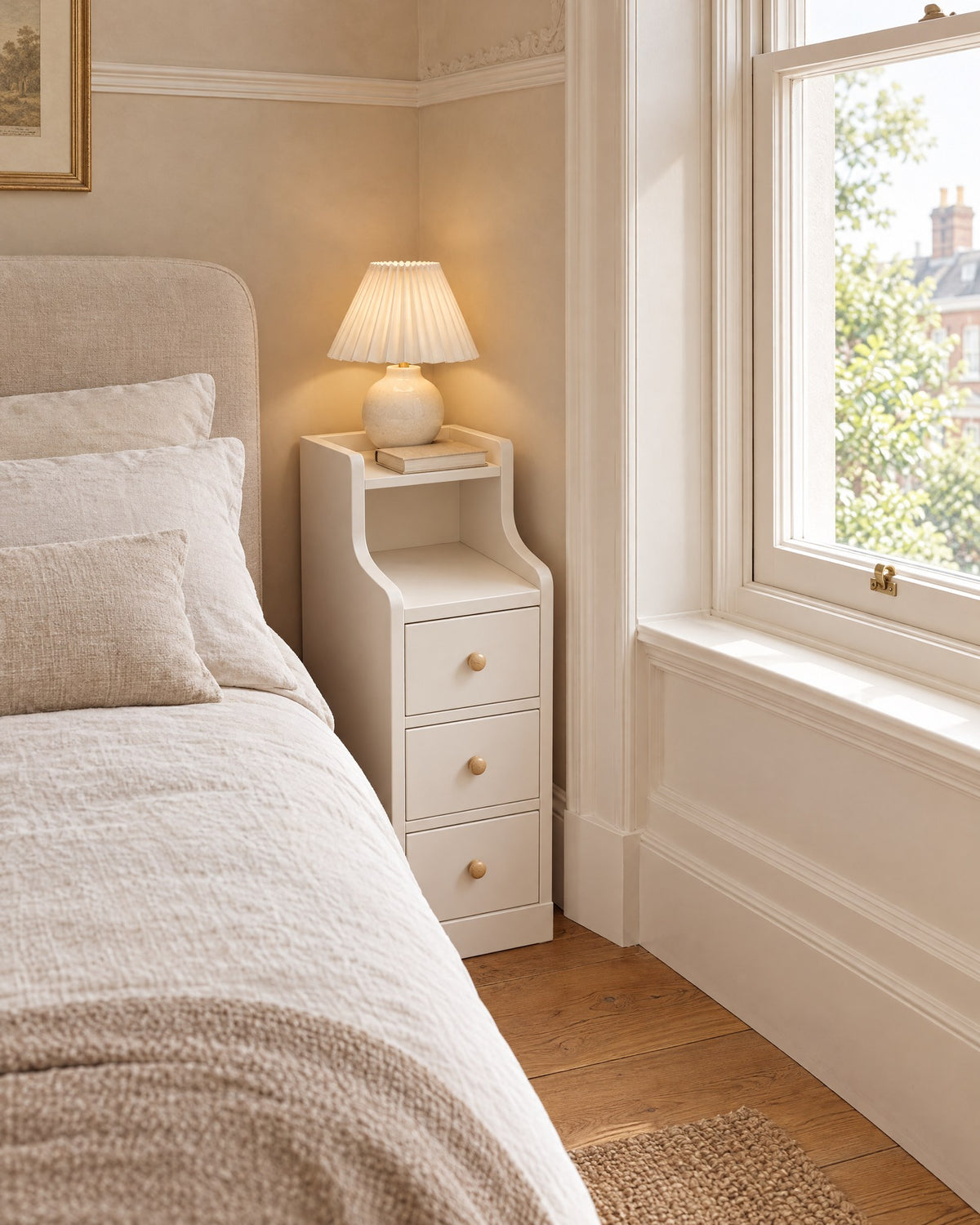Narrow 20 cm white bedside table beside a linen bed in a British bedroom with a sash window