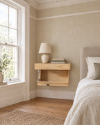 Natural wood floating bedside shelf beside a linen bed in a bright British bedroom with a sash window