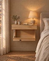 Natural wood floating bedside shelf fixed to the wall with a lamp switched on and an open book in the evening