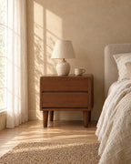 Nordic walnut bedside table with two handle-free drawers with a ceramic lamp in morning light