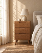 Oak bedside table with three drawers with a ceramic lamp in morning light