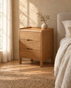 Three-quarter view of the oak bedside table showing its square legs and panelled side