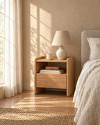 Oak bedside table with an open shelf and one drawer, with a ceramic lamp in morning light