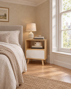 Oak-effect bedside table with open niche and white drawer beside a linen bed in a bright British bedroom with a sash window