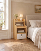 Oak-effect bedside table with open shelves and a lockable drawer beside a linen bed in a British bedroom with a sash window