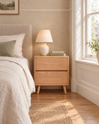 Oak bedside table with two drawers and tapered legs beside a linen bed in a British bedroom with a sash window