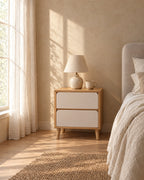 Oak and cream bedside table with two handle-free drawers with a ceramic lamp in morning light