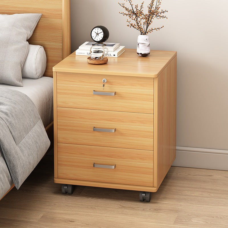 Oak-effect bedside cabinet with three drawers on castors beside a bed