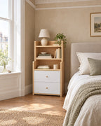Oak and white bedside table with hutch shelves beside a linen bed in a British bedroom with a sash window