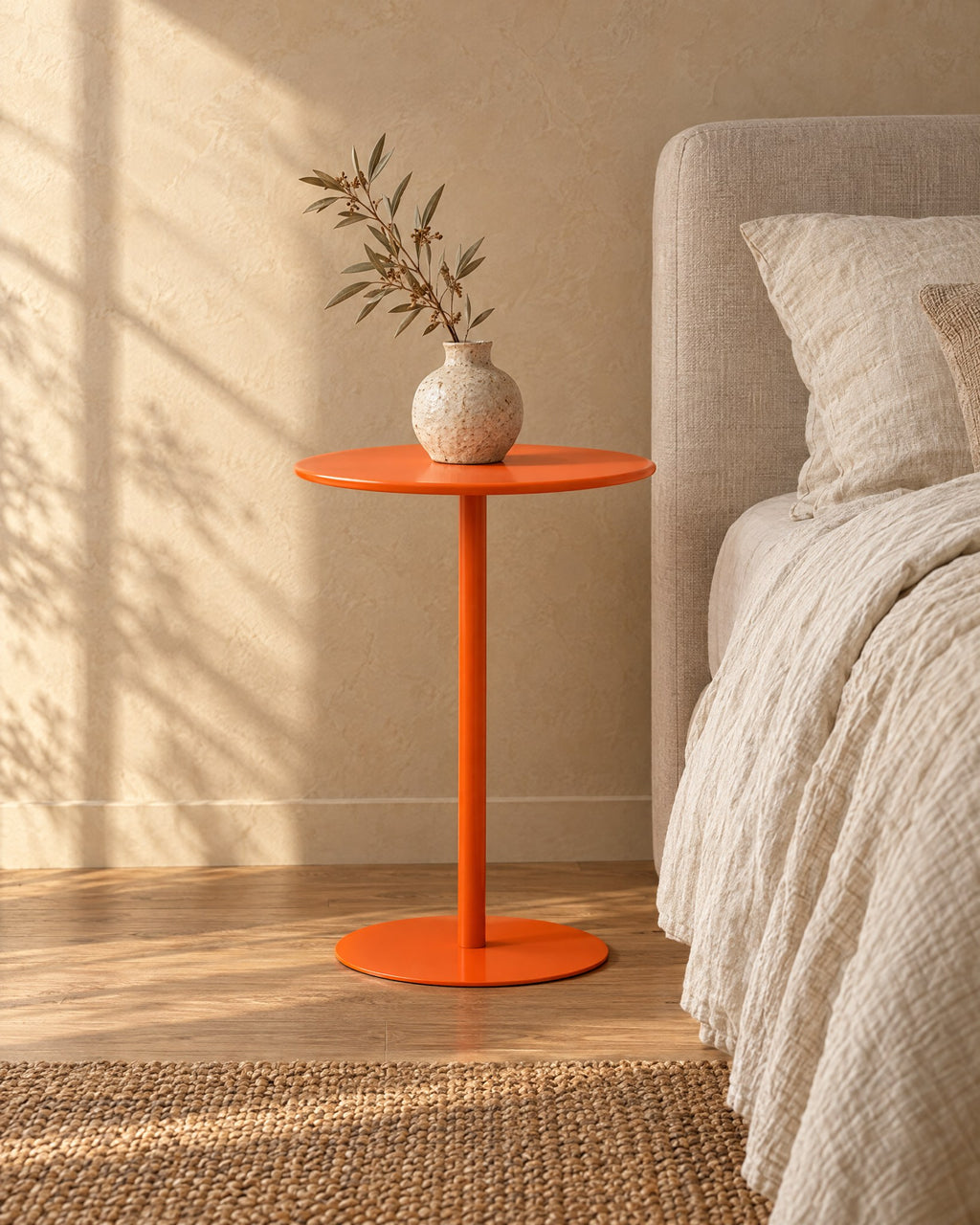 Three-quarter view of the orange metal pedestal side table beside the bed