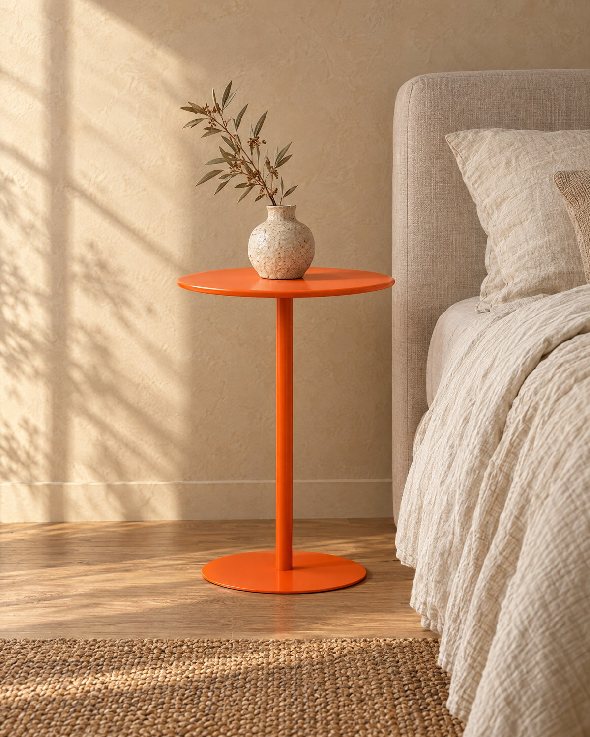 Three-quarter view of the orange metal pedestal side table beside the bed