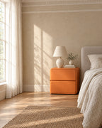 Orange rounded bedside table beside a linen bed in a British bedroom with a sash window