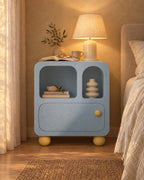 Pastel blue bedside cabinet with arched niches with a lamp switched on and an open book in the evening