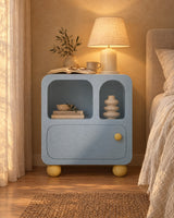 Pastel blue bedside cabinet with arched niches with a lamp switched on and an open book in the evening