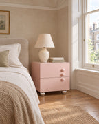 Pink Bedside Table beside a linen bed in a bright British bedroom with a sash window