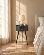 Round black bedside table with drawer in warm morning light with window shadows on the wall