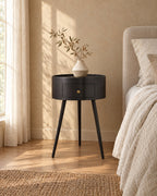 Three-quarter view of the round black bedside table with drawer beside the bed