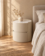Three-quarter view of the round cream bedside table standing on the floor