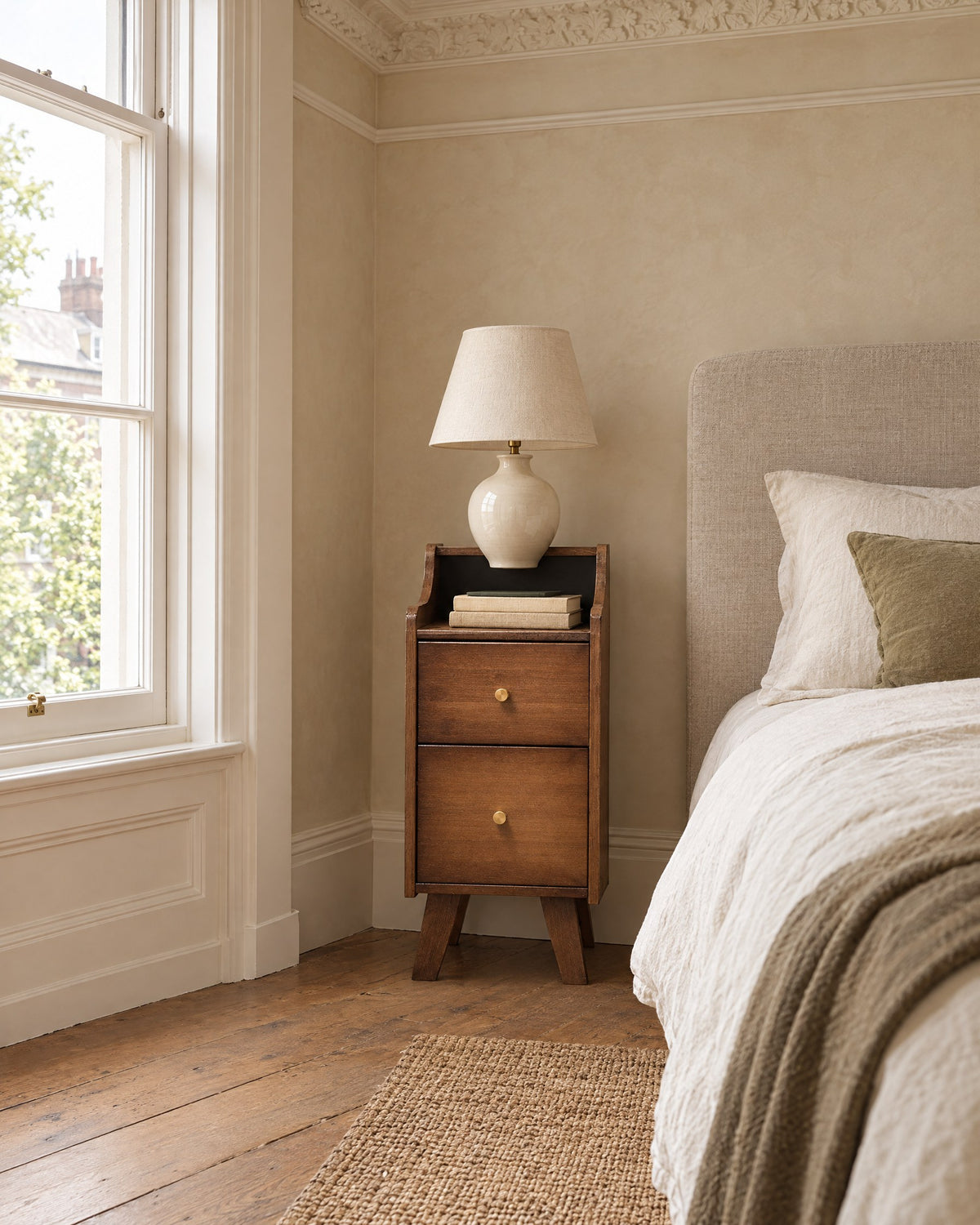 Slim walnut-finish bamboo bedside table beside a linen bed in a bright British bedroom with a sash window