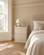 Slim cream bedside table beside a linen bed in a British bedroom with a sash window