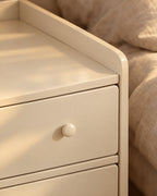 Close-up of the round knob of the top drawer and the raised rim of the cream bedside table