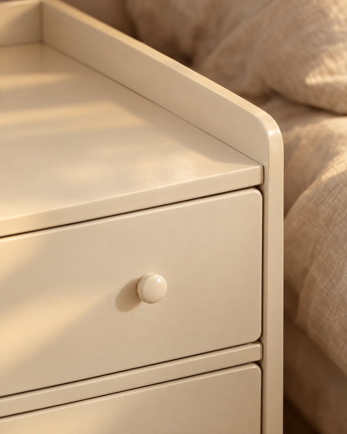 Close-up of the round knob of the top drawer and the raised rim of the cream bedside table