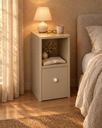 Slim greige bedside table with open shelf with a lamp switched on and an open book in the evening