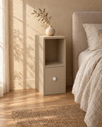 Three-quarter view of the slim greige bedside table with open shelf beside the bed