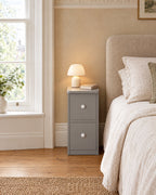 Slim grey bedside table beside a linen bed in a British bedroom with a sash window