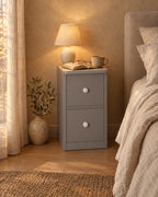 Slim grey bedside table, lamp switched on and an open book in the evening
