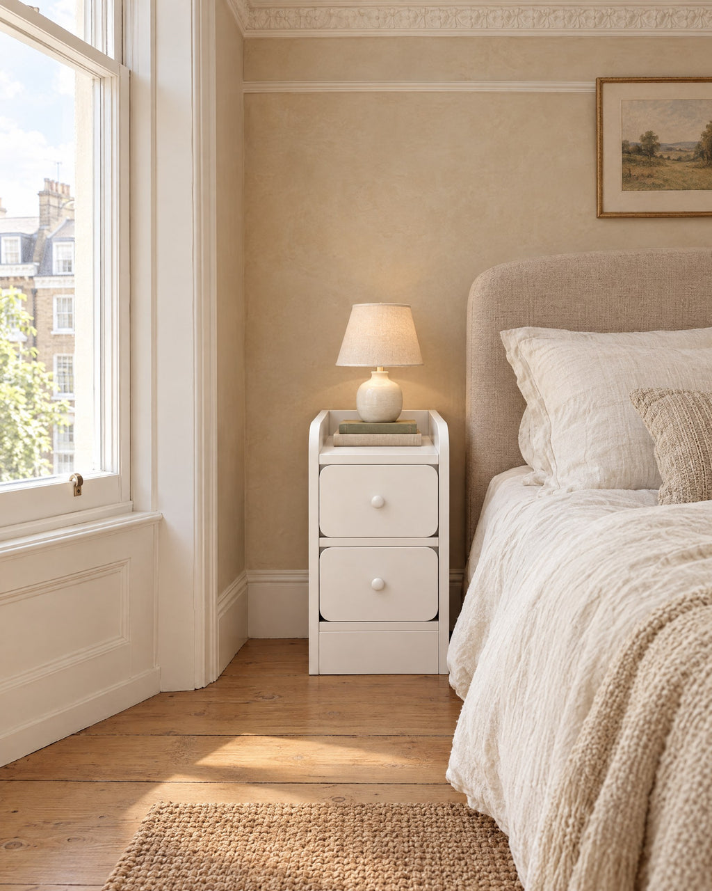 Slim white bedside table in the narrow gap beside a bed in a British bedroom