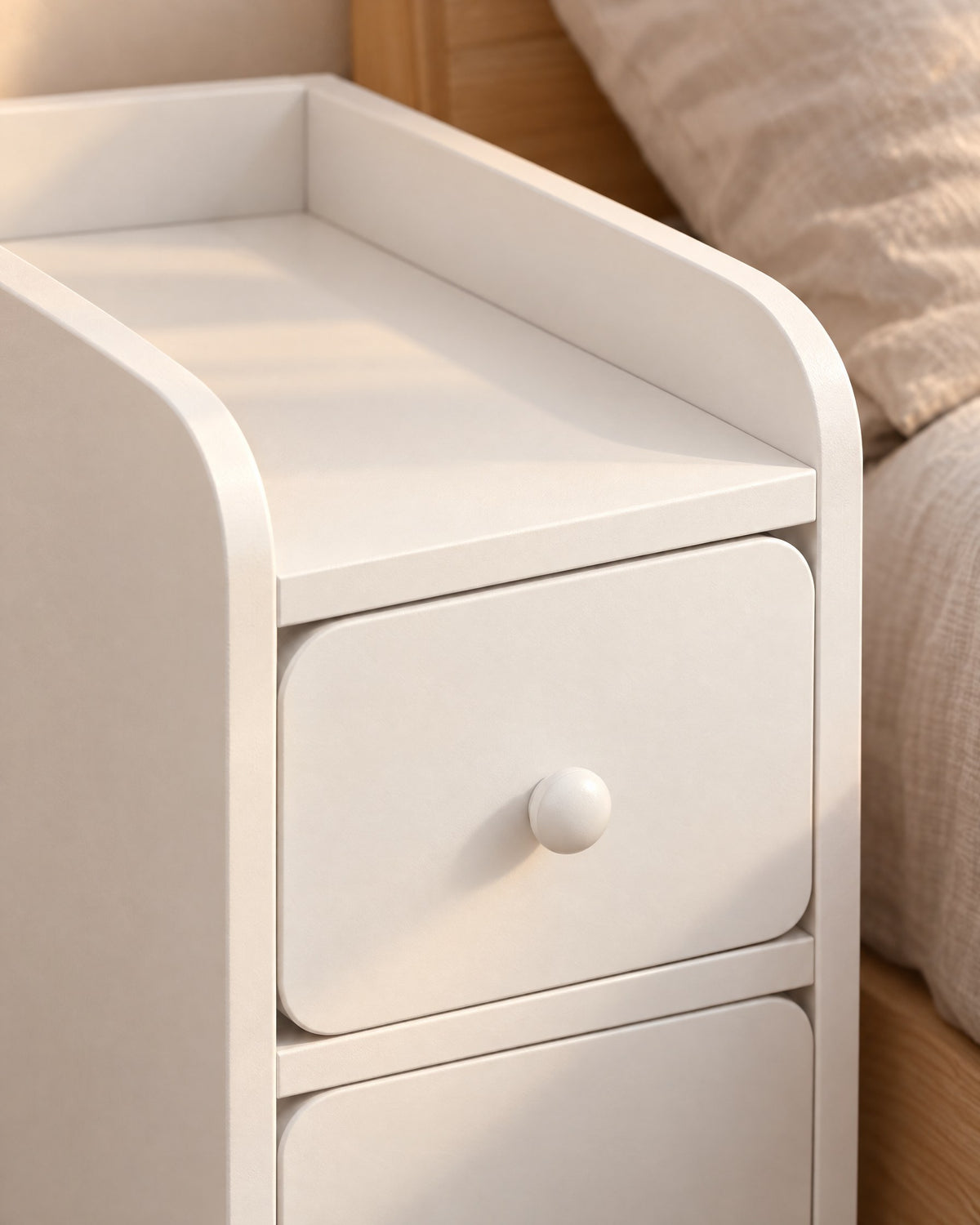 Close-up of the round knob, rounded drawer and raised rim of the white bedside table