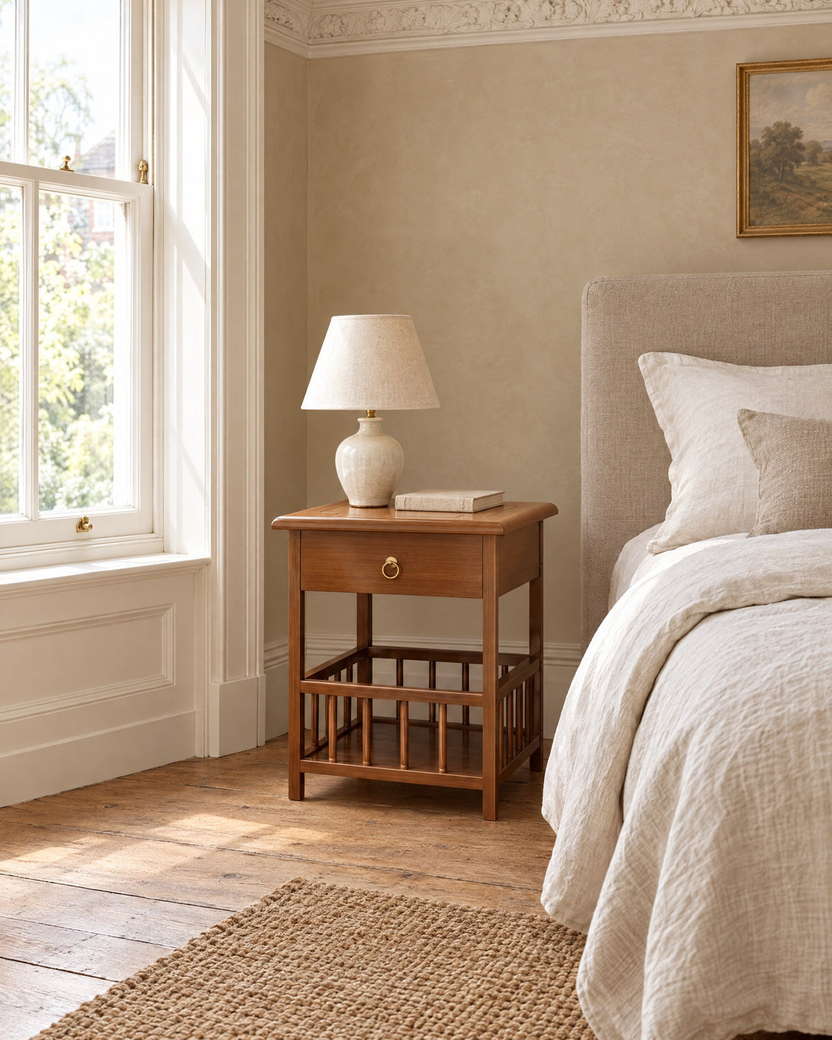 Small bamboo bedside table beside a linen bed in a British bedroom with a sash window