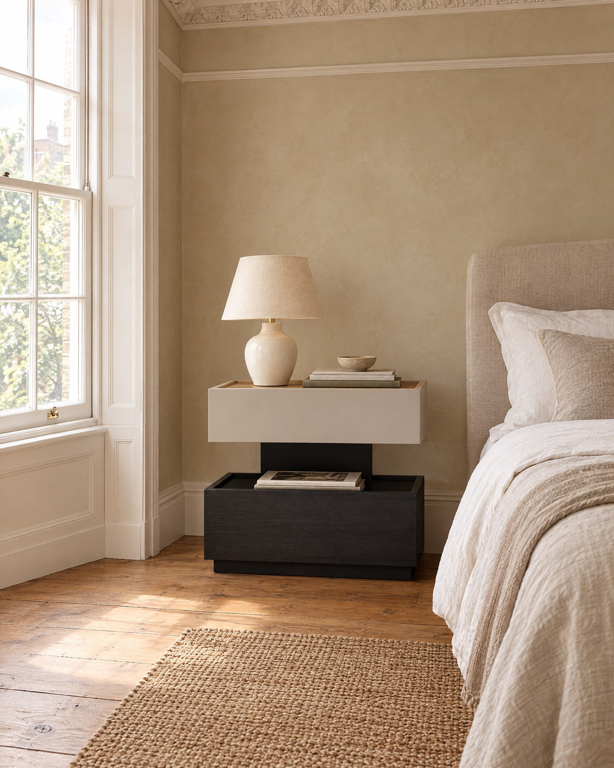 Two-tier greige and black bedside table beside a linen bed in a British bedroom with a sash window