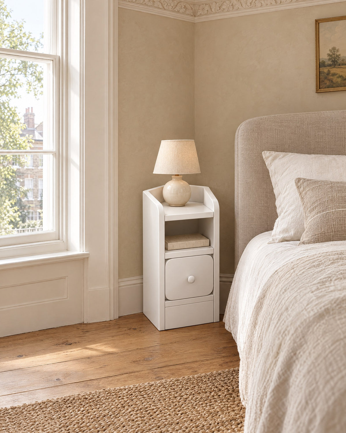 Ultra-narrow white bedside table beside a linen bed in a British bedroom with a sash window