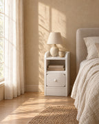 Narrow white bedside table with a ceramic lamp in morning light