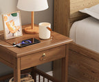 Walnut-tone bamboo bedside table with a drawer and a phone on the top beside a bed