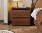 Walnut bedside table with black top and two drawers beside a bed