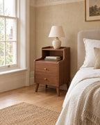 Walnut bedside table with open shelf beside a linen bed in a British bedroom with a sash window