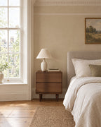 Walnut bedside table beside a linen bed in a British bedroom with a sash window