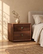 Three-quarter view of the walnut bedside table with a fluted drawer and clover knobs