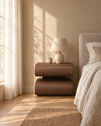Walnut bedside table with curved drawers and a ceramic lamp in morning light