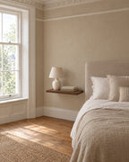 Walnut floating bedside shelf beside a linen bed in a bright British bedroom with a sash window