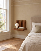 Walnut fold-down wall bedside shelf beside a linen bed in a bright British bedroom with a sash window